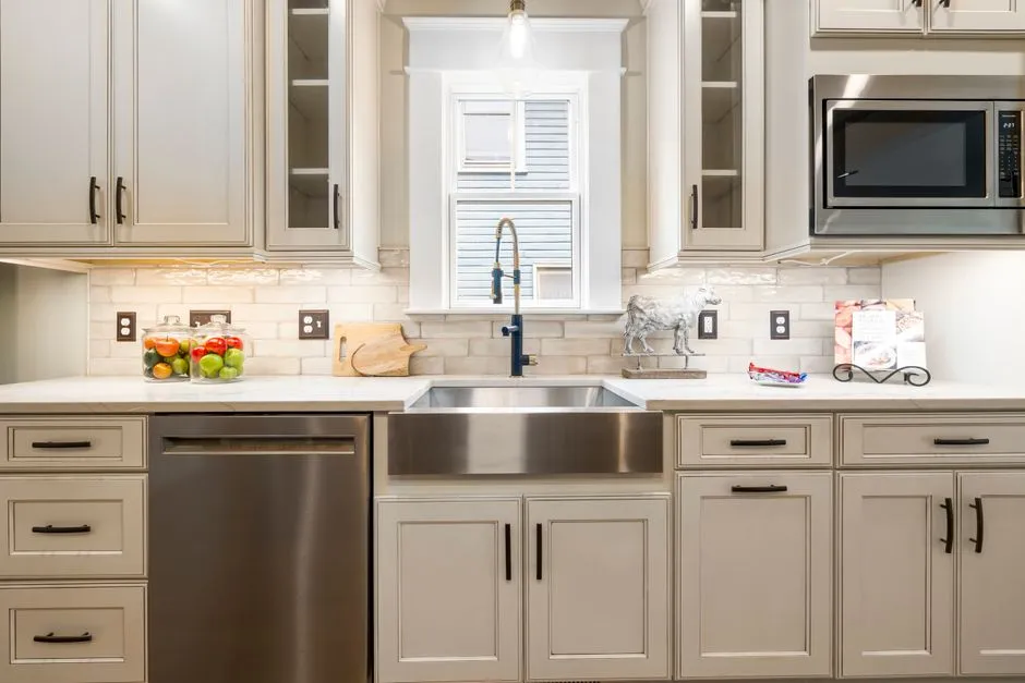Farmhouse-style kitchen with pale cream cabinets, a stainless farmhouse sink, and tile backsplash